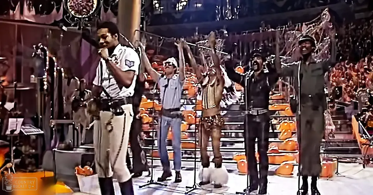 A musical performance in an indoor arena or concert hall with a crowd of spectators, stage lighting equipment, and a mix of uniformed and casual attire.