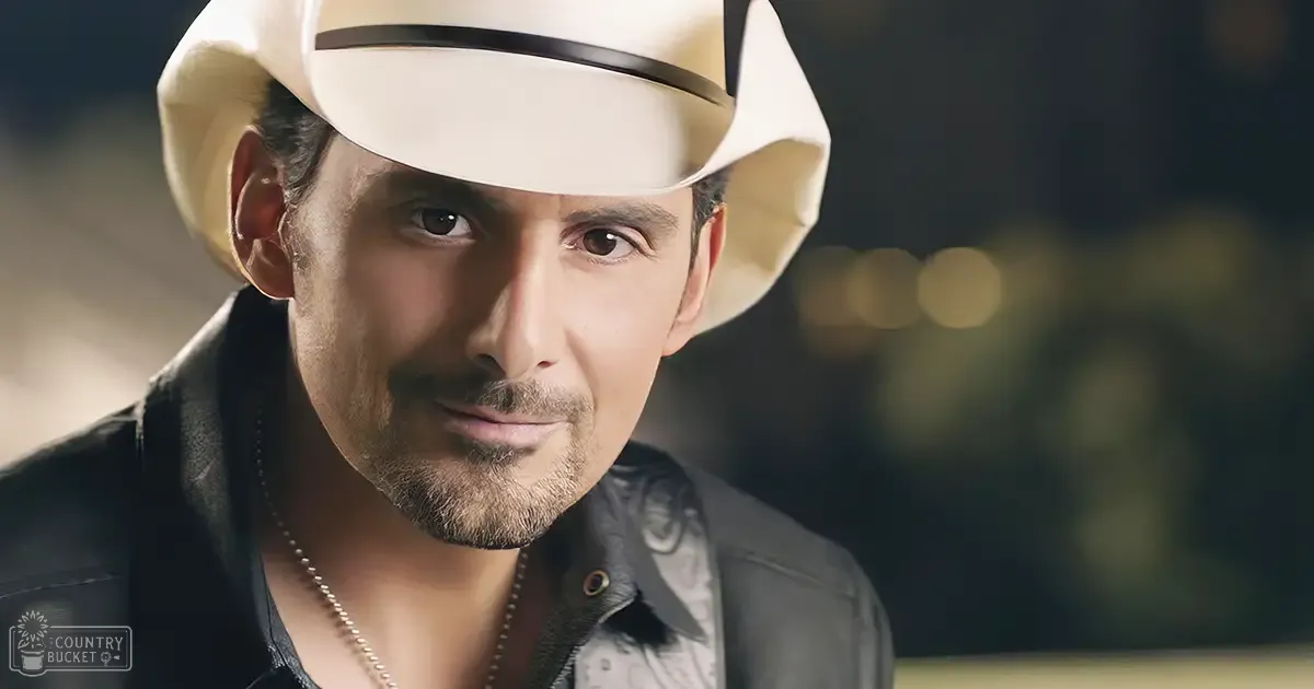 A middle-aged adult male wearing a black leather jacket with white cowboy hat and silver necklace, set against an urban evening backdrop.