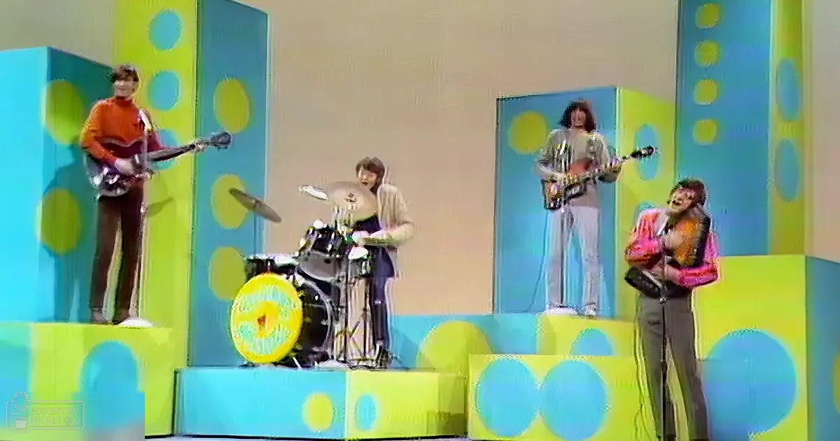 Musical performance on an indoor stage with polka-dotted panels in blue and yellow, with electric guitars, drums, and tambourine.