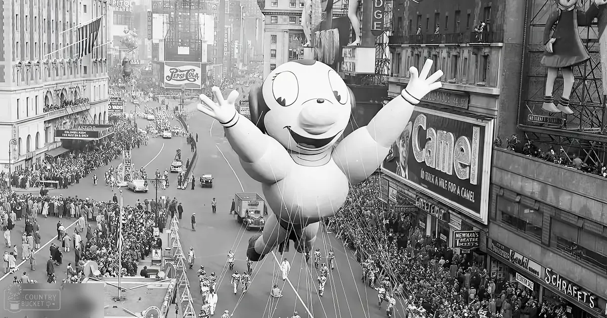 A vibrant parade scene in Times Square, New York City, during spring or summer with clear daylight. Vintage cars line the street, and an inflatable character stands as a central focus among spectators dressed in mid-20th century attire.