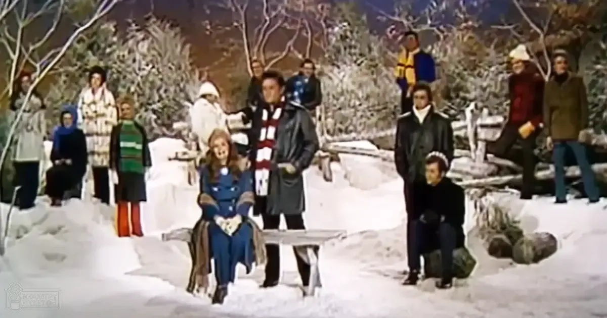 Group photo of adults and a child in winter attire, seated and standing outdoors on a snowy day with overcast light.