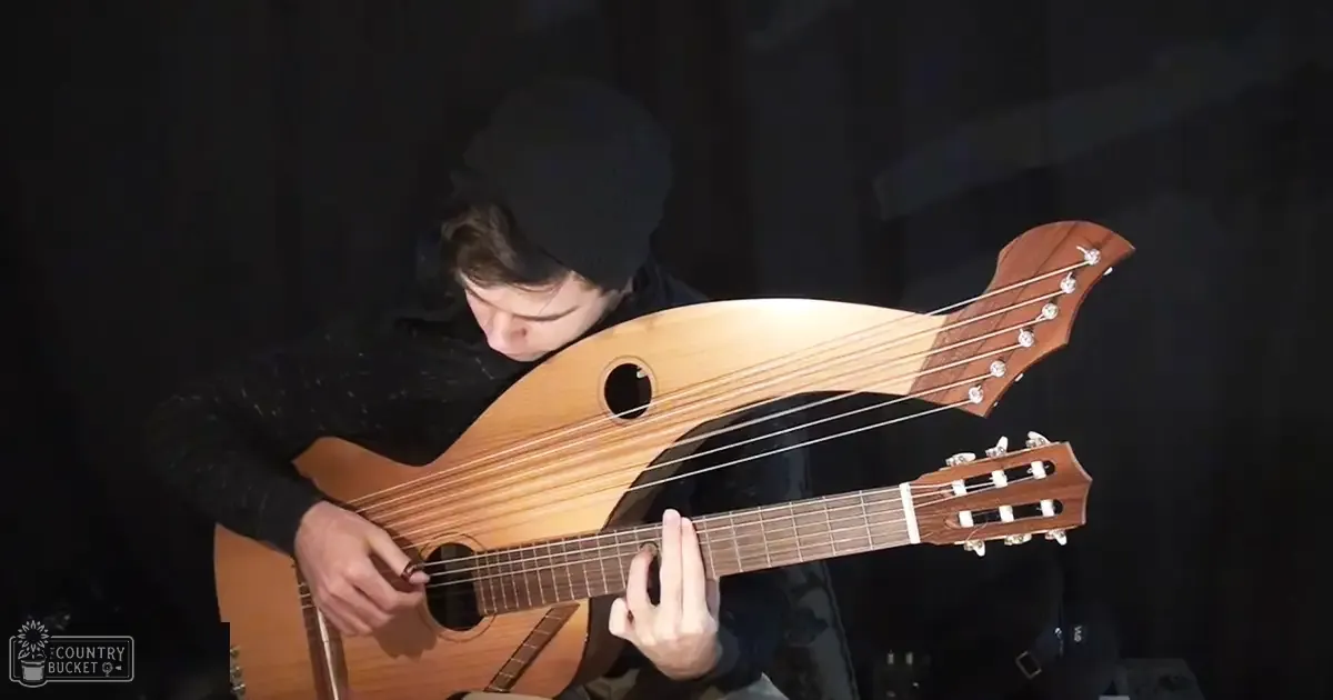 A young adult male playing an unusual stringed instrument in a dimly lit studio setting.