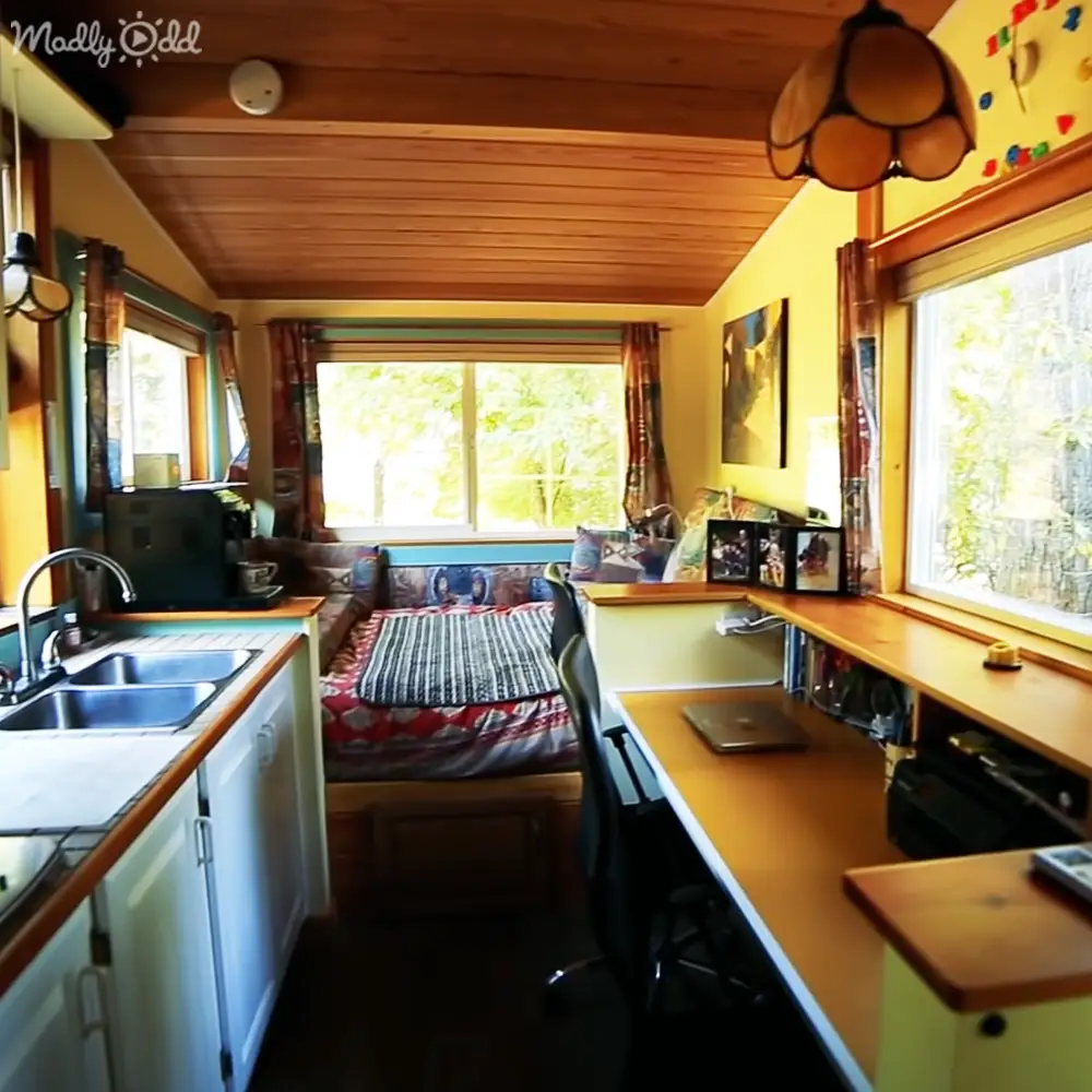 A cozy, compact living space with white cabinets, wooden countertops, and colorful bedding in a van or small home during spring or summer with ample natural light.
