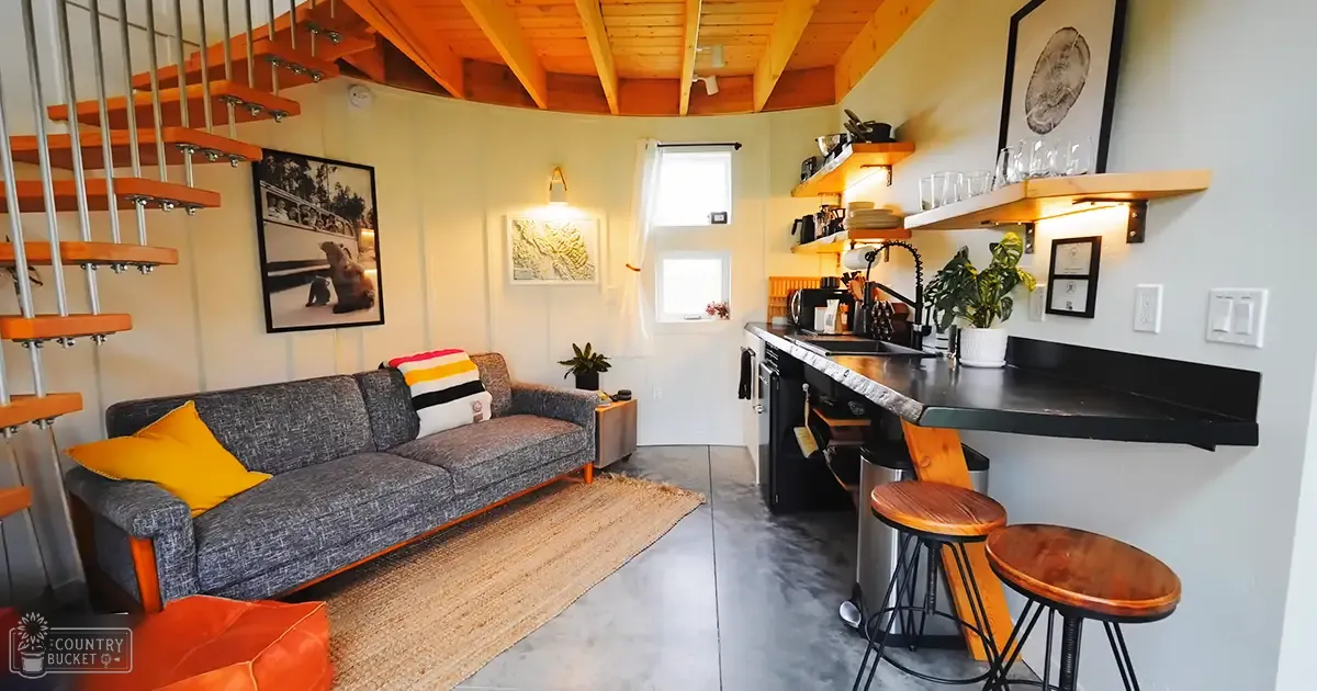 A cozy indoor living space with a gray sofa, orange staircase, wooden shelves, and framed artwork depicting an animal.