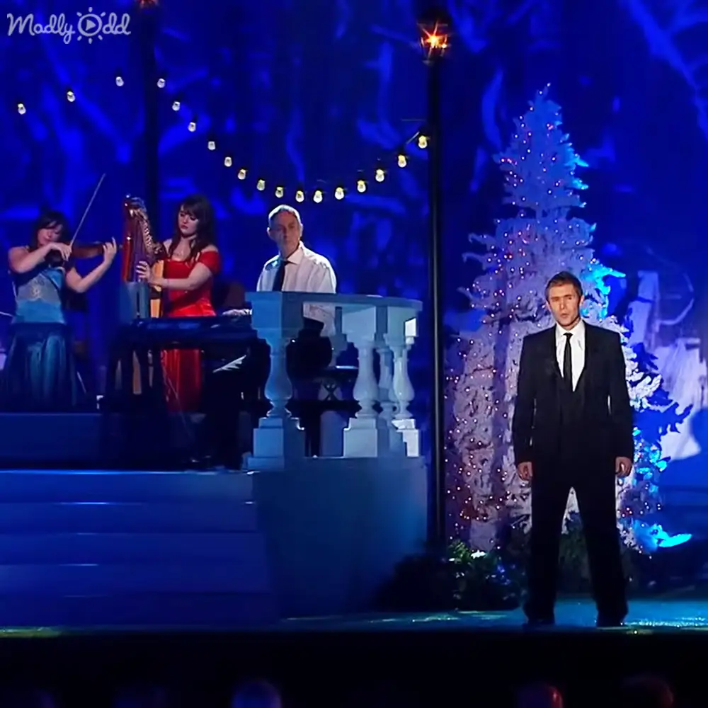 Indoor performance venue with string lights and a decorated Christmas tree, dark blue lighting creating dramatic effect typical of stage performances.