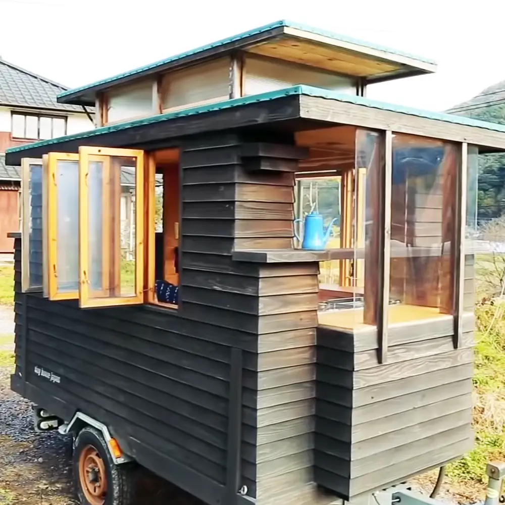 A small rural mobile home with a blue watering can on display in an outdoor setting during late afternoon or early evening light.