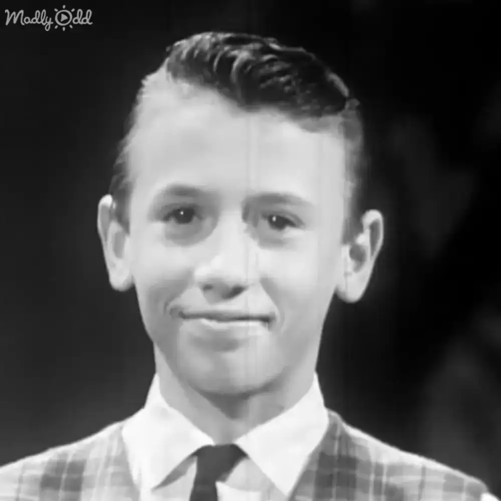 Young adult male in a plaid shirt with a white collared undershirt, dark tie, and regular fit, standing indoors against a dark background.