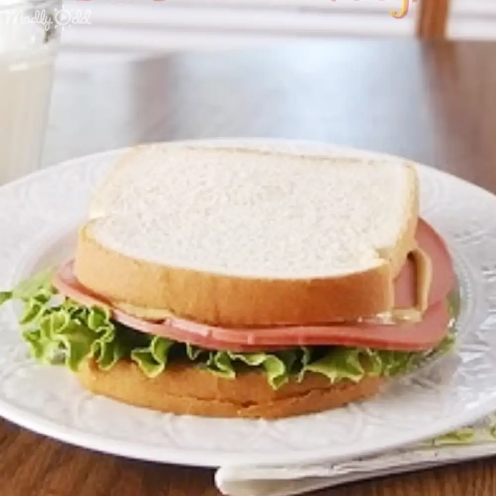 A sandwich with lettuce, ham, and possibly mayonnaise on a white plate in a kitchen setting.