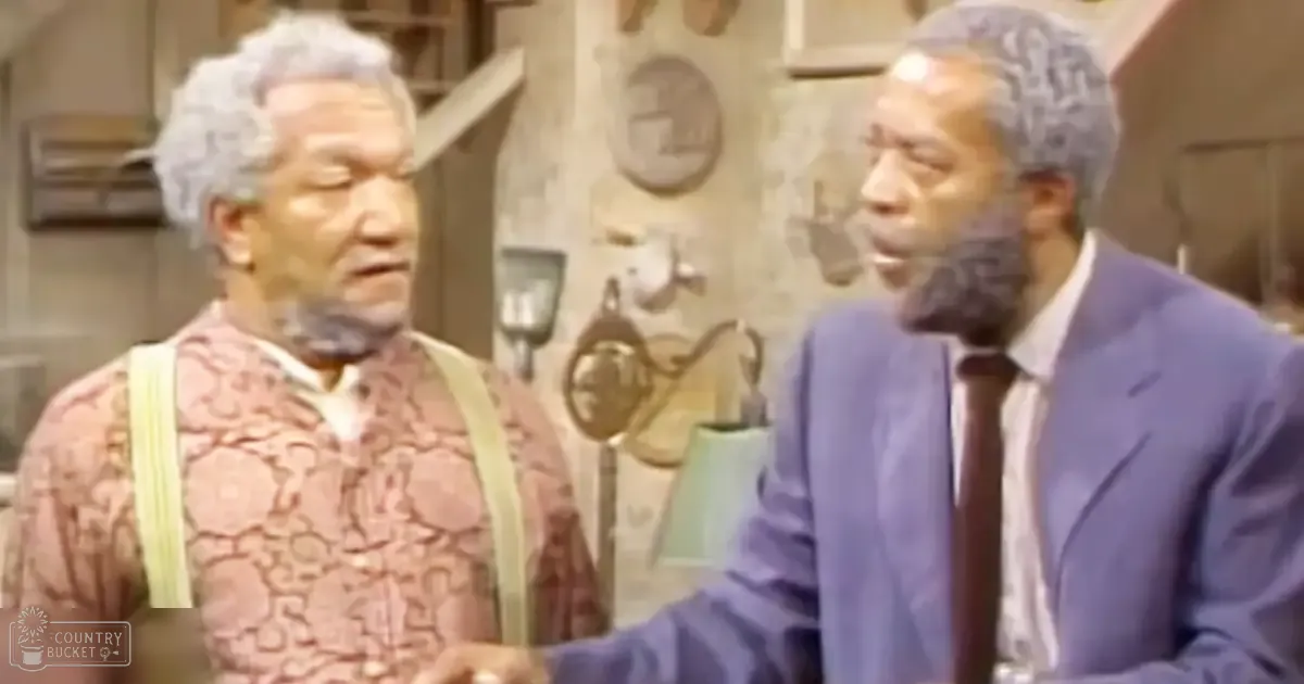 A comedic scene from a television show or film set indoors with two adult males wearing patterned sweater and mid-20th century suit in casual environment.