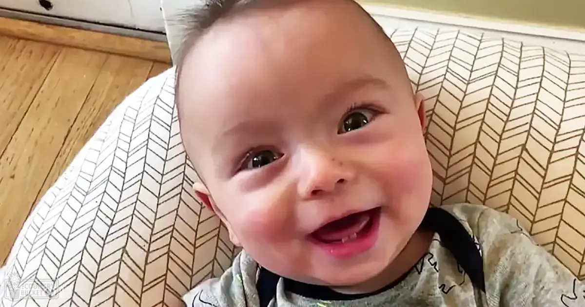A baby in a green onesie with an abstract pattern, indoors under natural light.