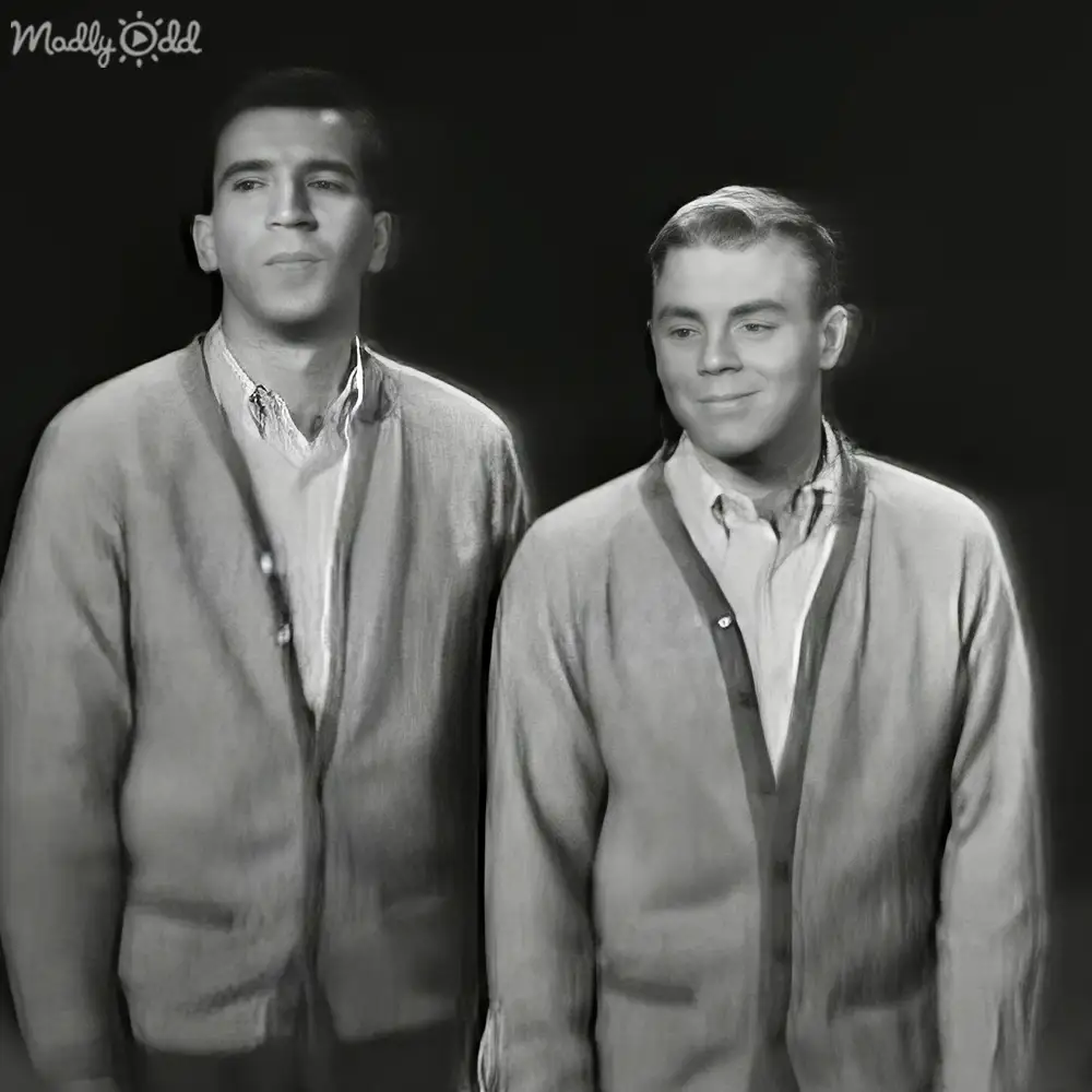 Two young adult males in a studio setting, wearing open cardigan sweaters with collared shirts underneath.