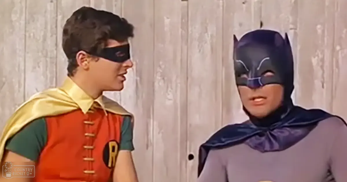Batman and Robin in a classic 1960s superhero setting with wooden backdrop, likely spring or summer daylight scene.