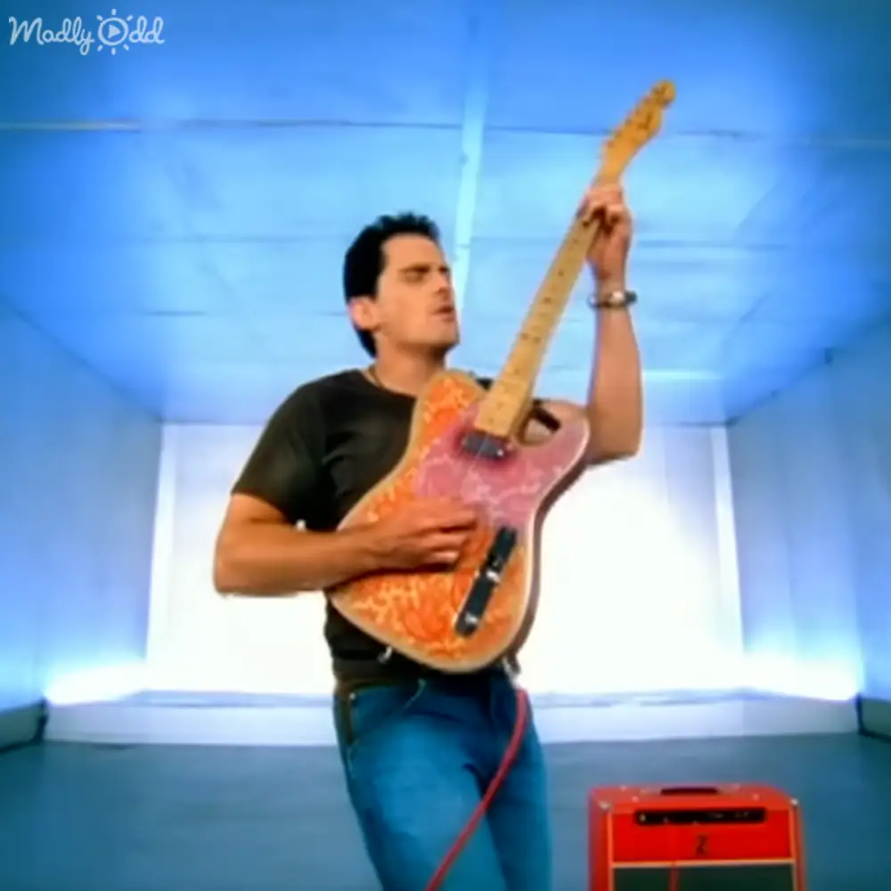 A young adult male playing a guitar indoors with a blue wall background.