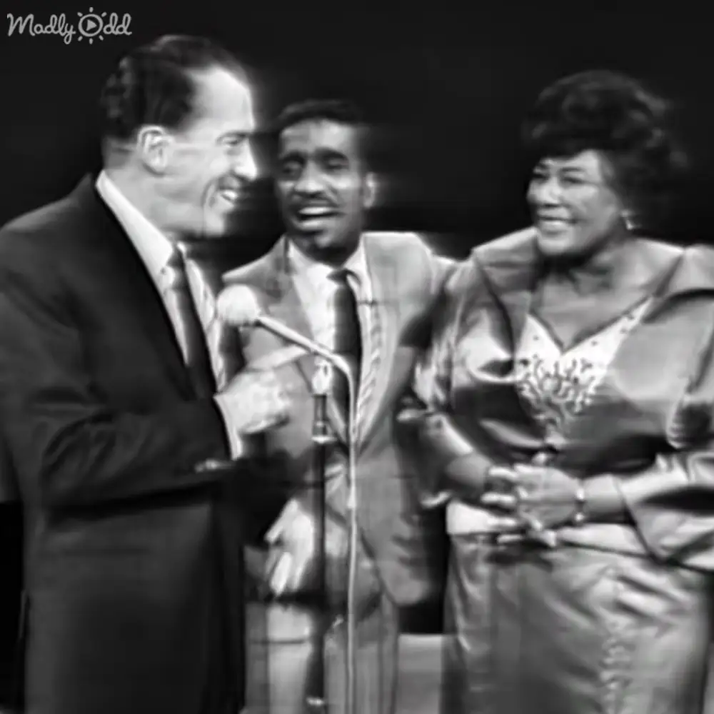 A musical performance scene with three adults in formal attire on stage under dim lighting.