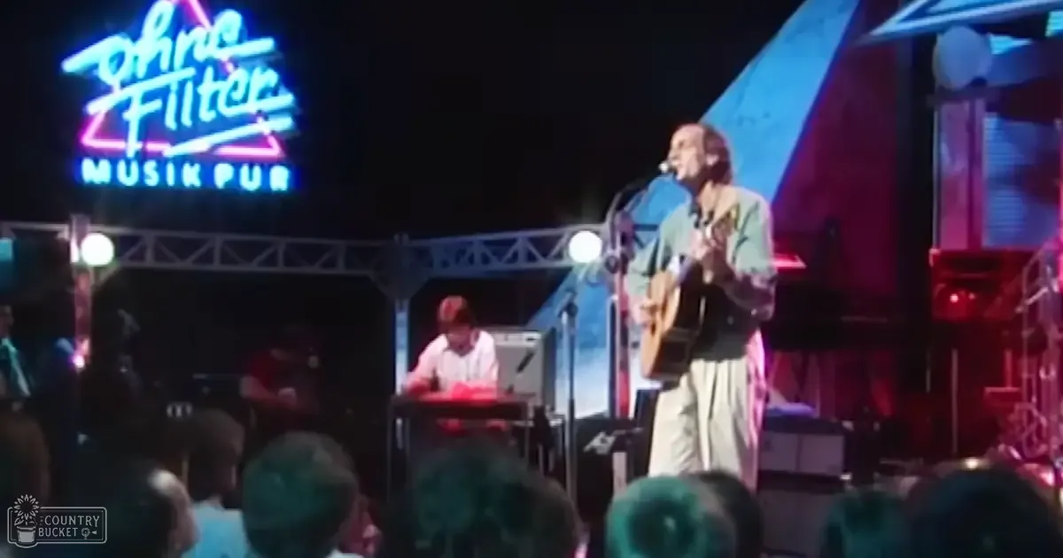 A musician with light-colored hair and a green and beige shirt performs at an outdoor concert at Dine Filter Musik Pub under red and blue stage lights.