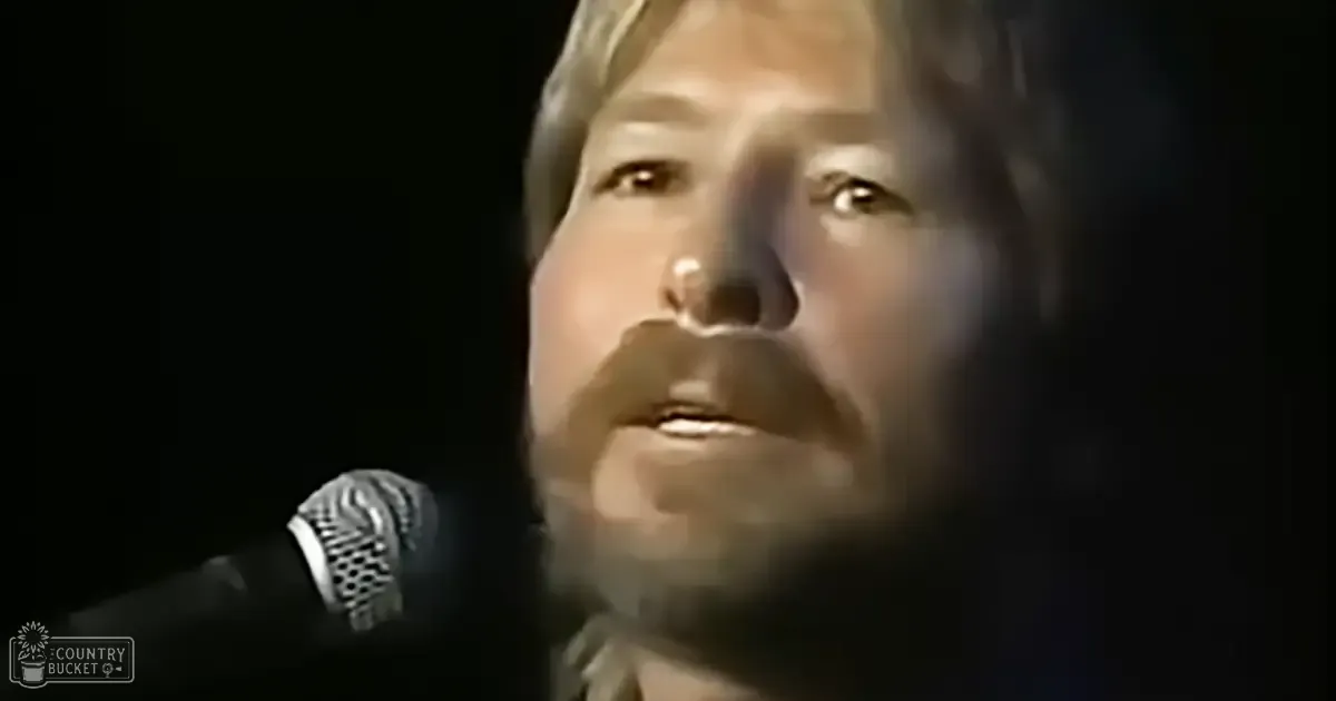 A middle-aged man singing into a vintage microphone in an indoor setting under dramatic lighting.