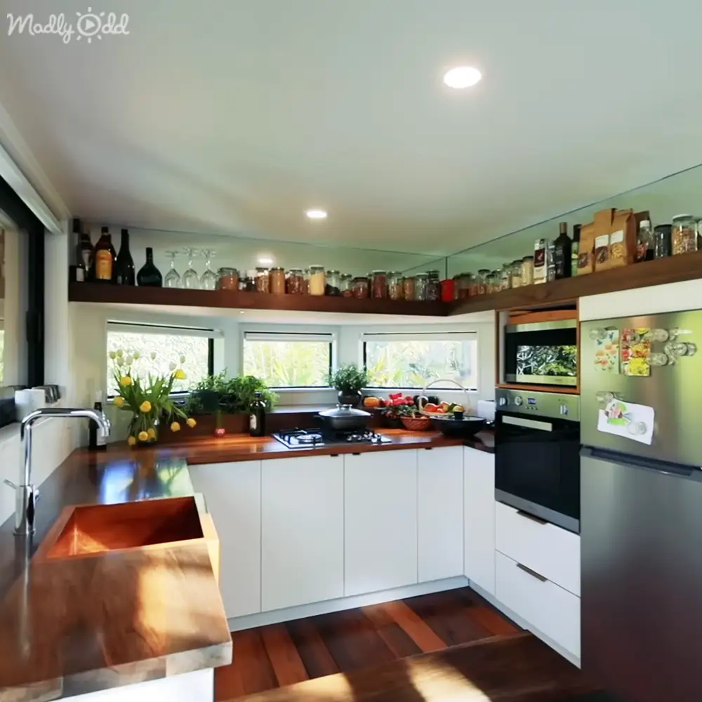 A residential kitchen with wooden countertops, a copper sink, white cabinets, an oven with microwave above it, and a stainless steel refrigerator on the right side of the image.