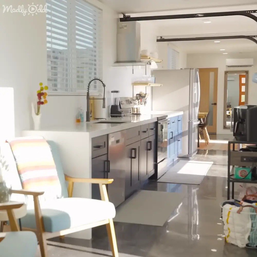 Modern kitchen with white chair, blue cabinets, black entertainment stand and colorful flowers indoors during daytime in a residential home.