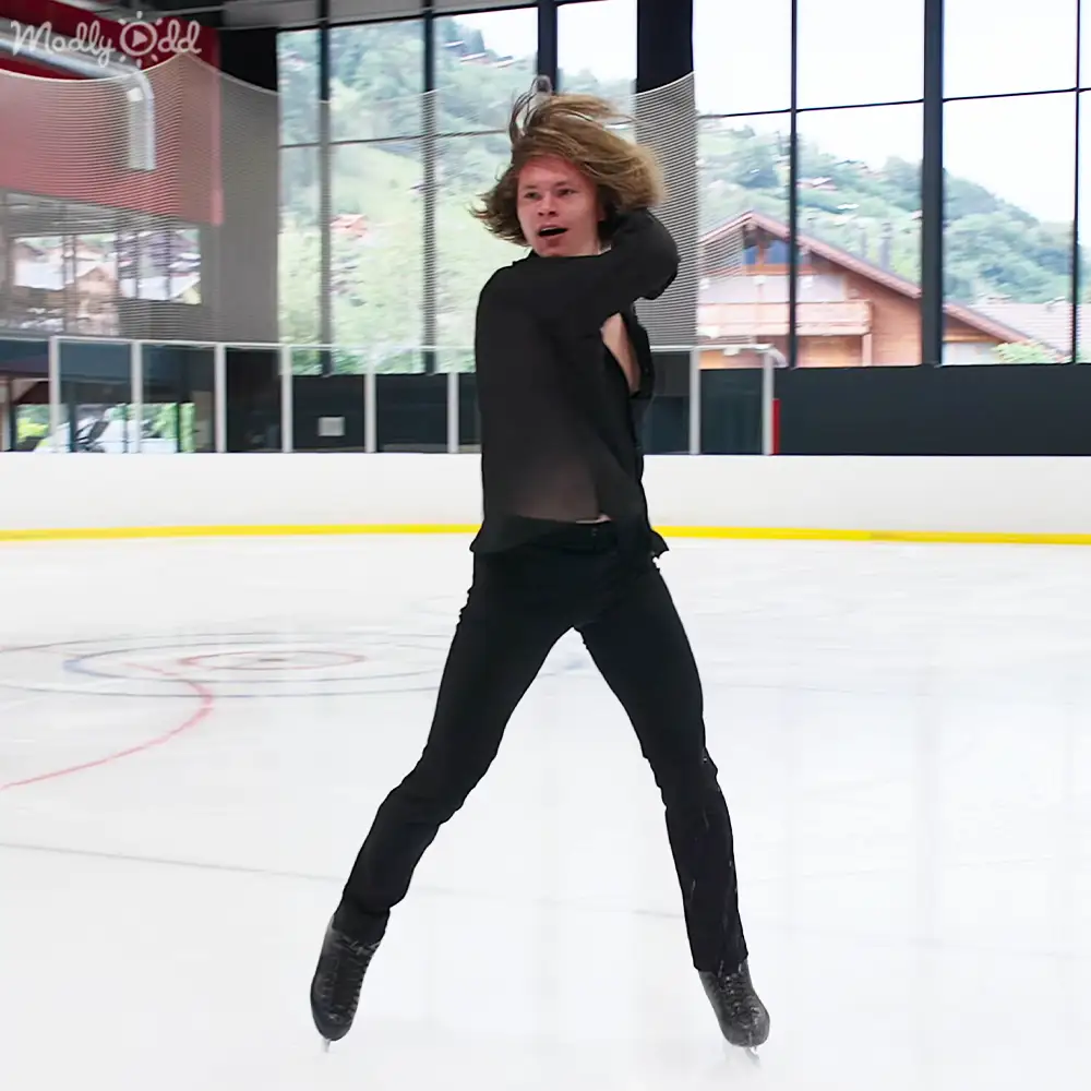 A young adult male skates indoors, surrounded by mountainous scenery visible through large windows on a sunny day.