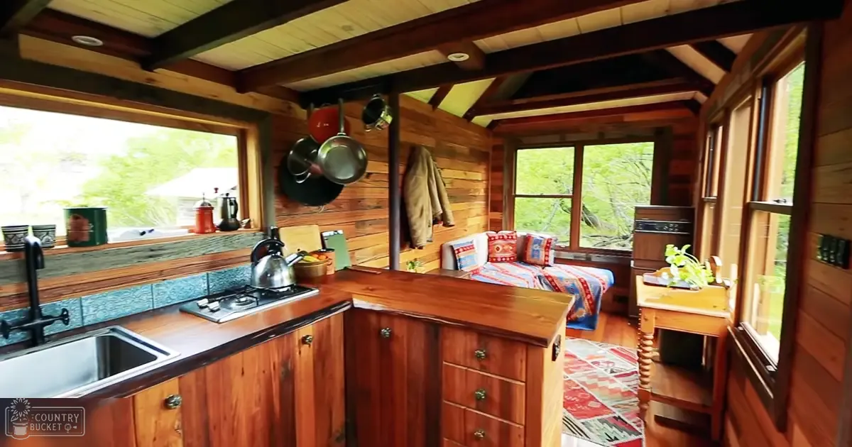 Cozy cabin interior with wooden furniture and colorful bedding, natural light filtering through windows showing greenery outside.