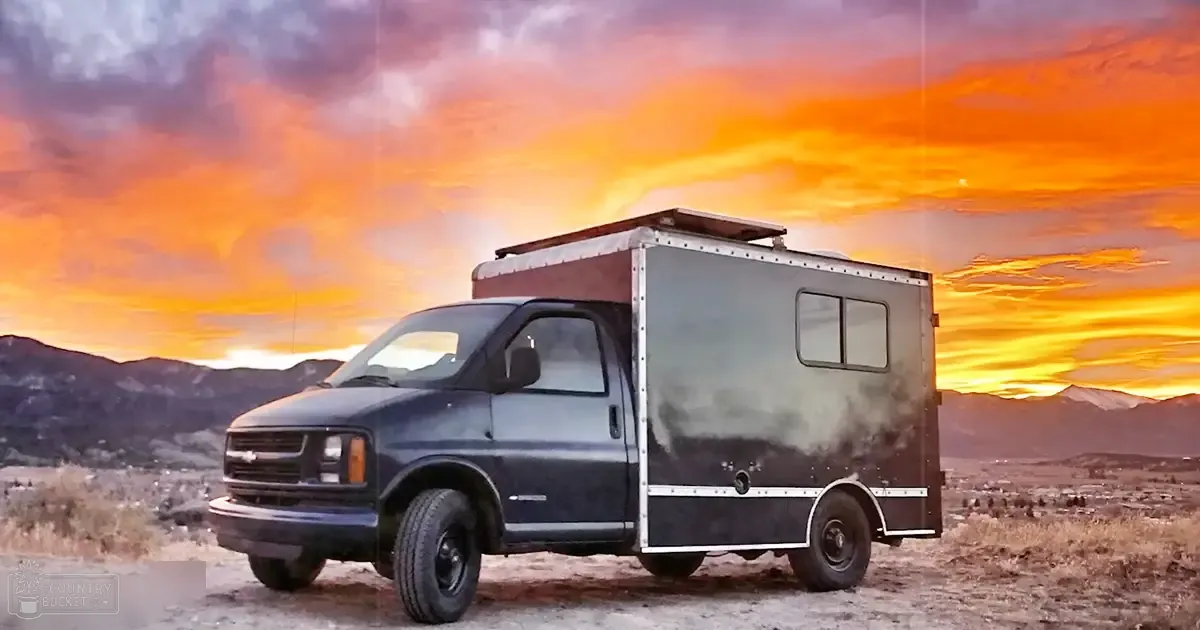 A converted black Chevrolet van in a desert-like environment during sunset.