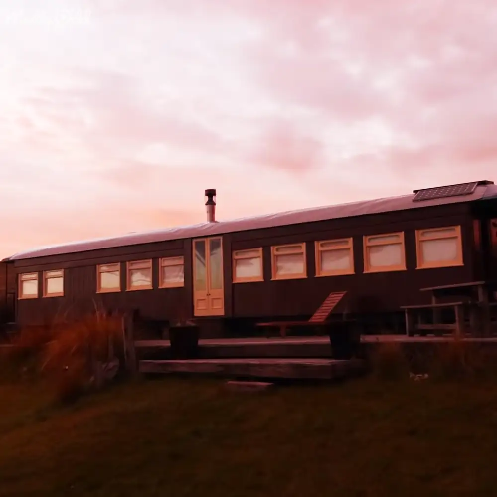 Repurposed train car converted into a home in a rural countryside setting with wooden furniture and a solar panel at twilight.