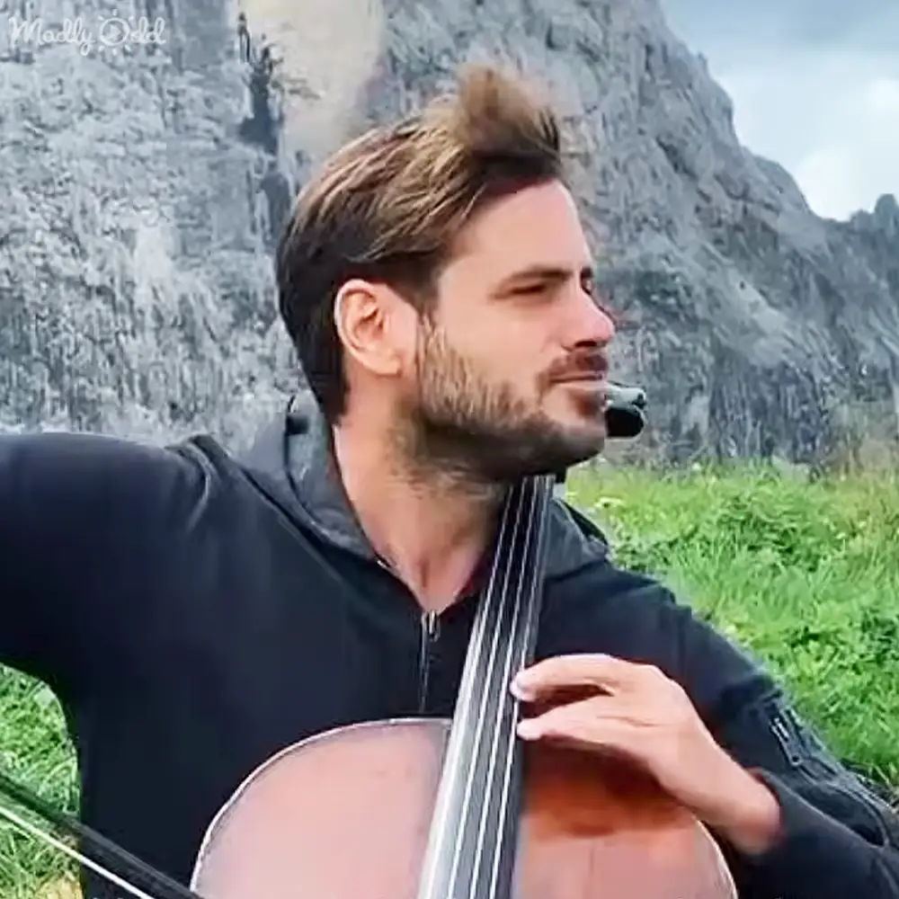 Adult male playing a cello outdoors with mountains in the background, late afternoon light, spring or summer season.