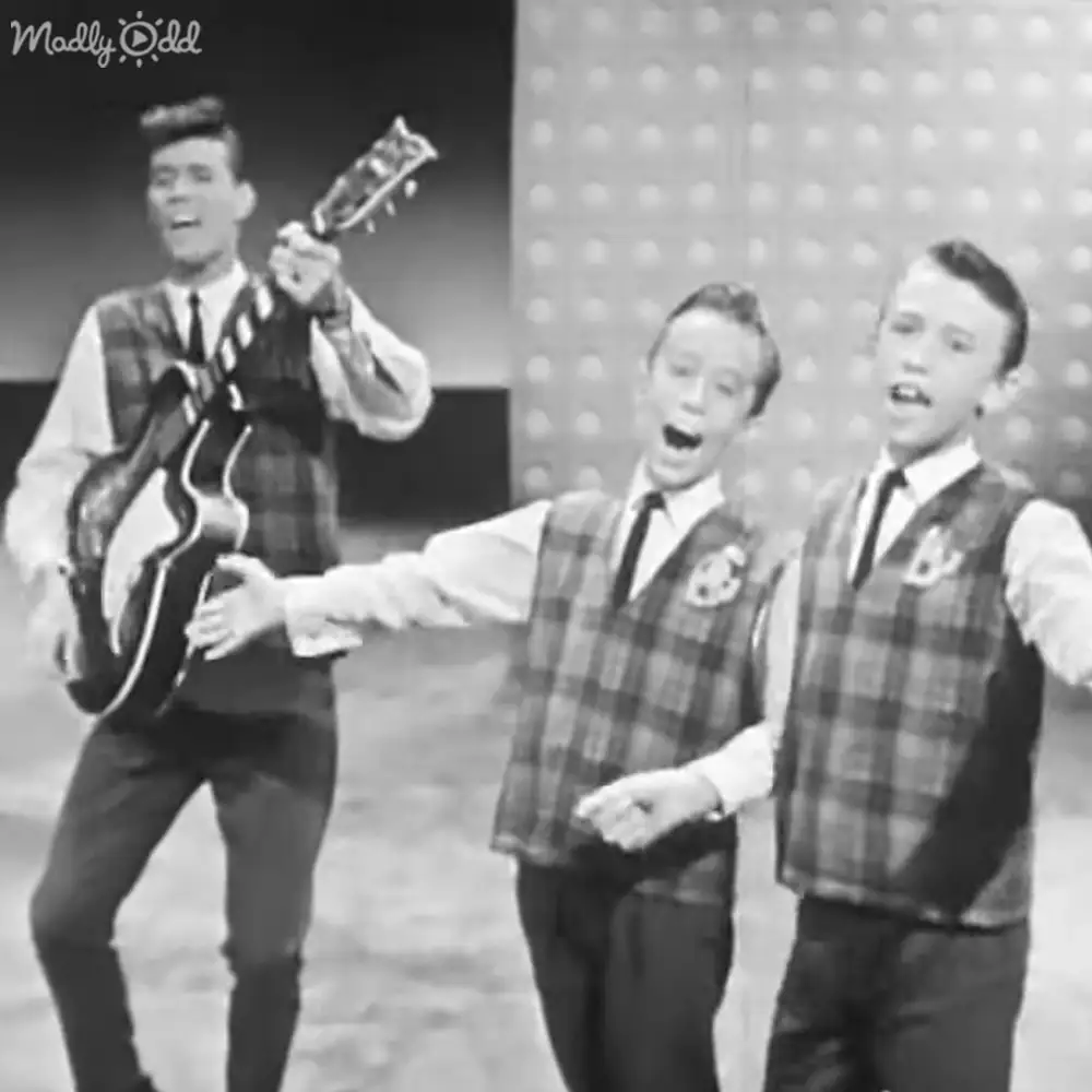 Young adult males perform on a mid-20th-century stage with plaid vests and white shirts, suggesting a musical variety show.