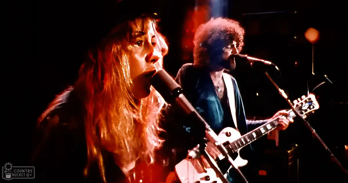 A young adult female in a dark blue, fitted long-sleeved garment performs alongside an older male in similar attire at night under stage lights in a small indoor venue.