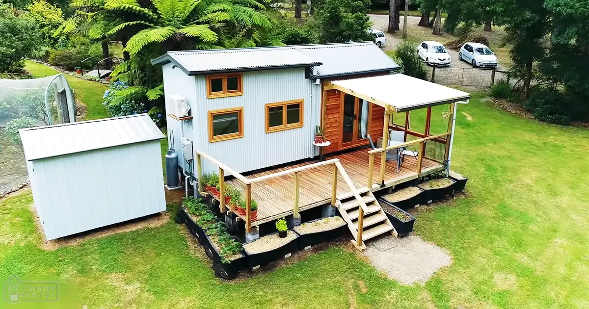 A suburban residential area with a small house with light blue siding, wooden deck, and potted plants on a sunny day.