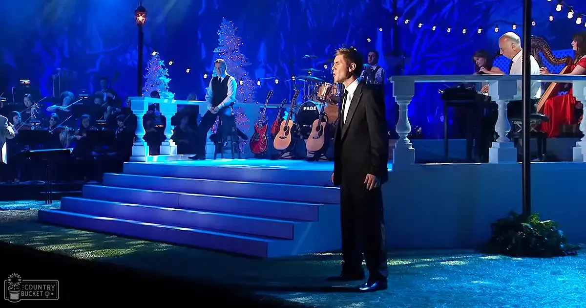 An indoor concert setting with blue lighting, a row of guitars, and a decorated Christmas tree in a festive scene.