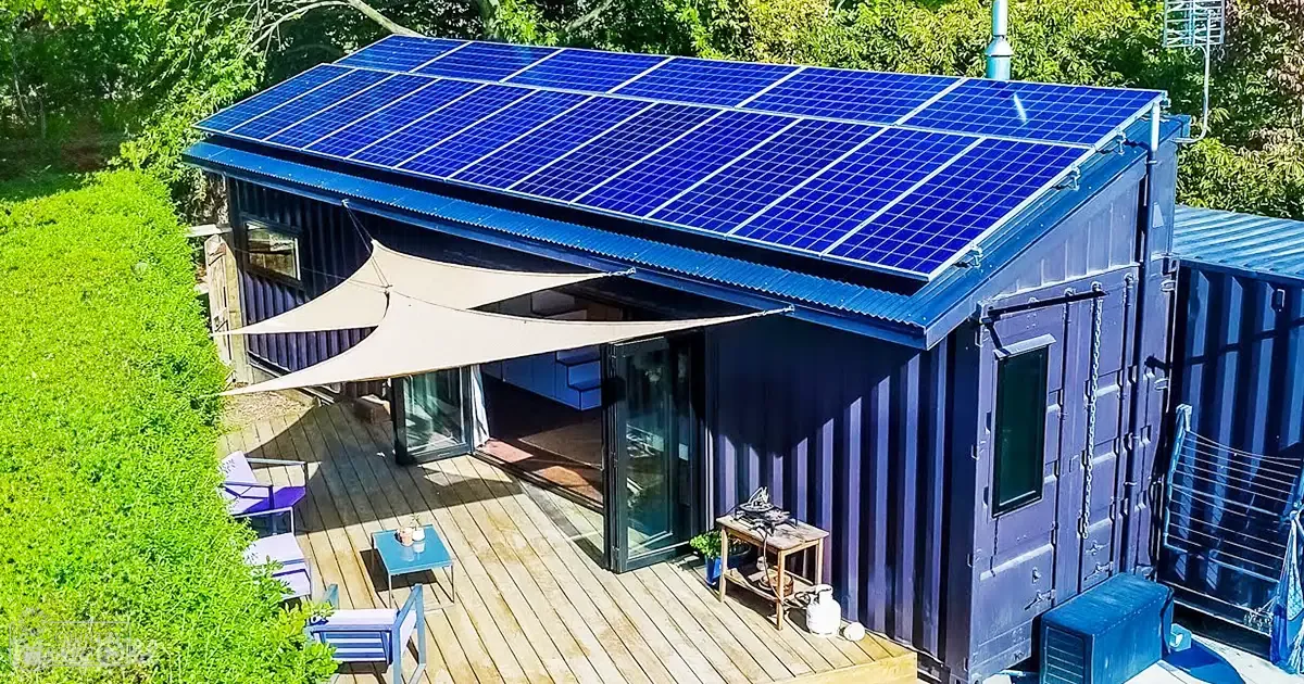 Solar-powered building made from shipping containers, surrounded by greenery on a sunny day in spring or summer.