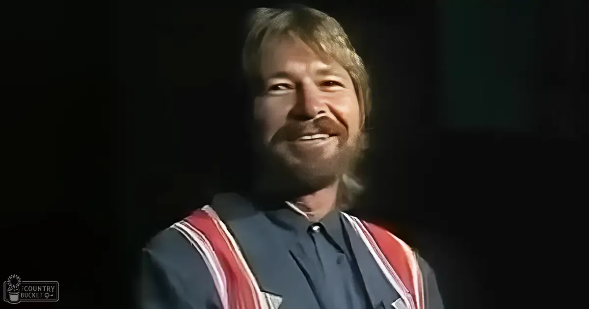 A middle-aged adult male wearing a dark blue collared shirt and holding a red and white striped sash in an indoor setting with dim lighting.