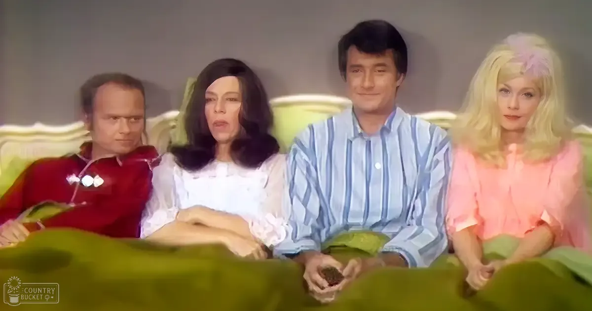 A group of middle-aged individuals seated together indoors, wearing various casual and semi-formal attire in a plain setting with even lighting.