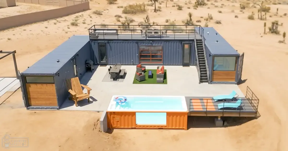 A modern shipping container home in a desert setting with hot tub, wooden furniture, and outdoor seating.
