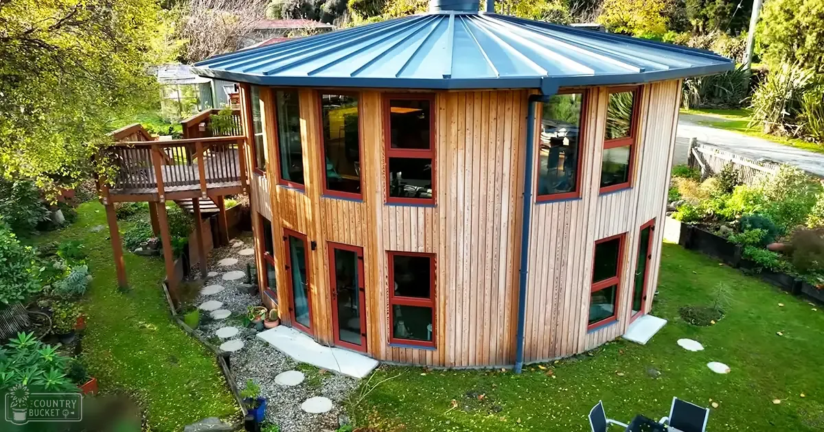 A suburban house with a blue roof, wooden deck, and lush greenery in daylight.