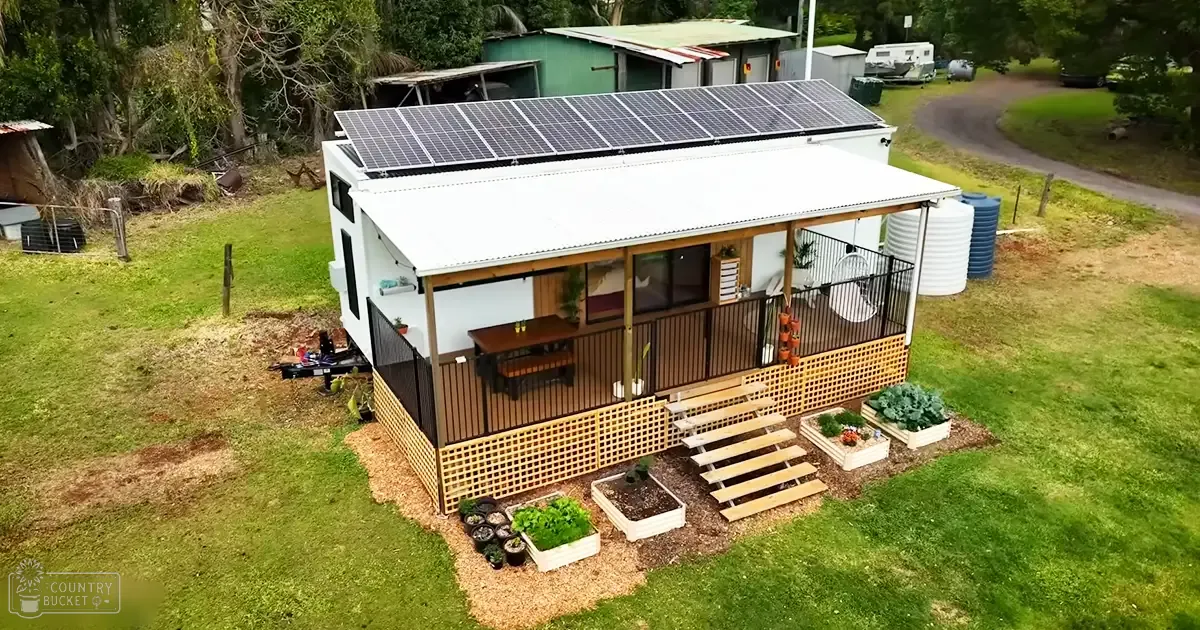 Rural setting with a modern house, solar panels, wooden furniture, greenery, spring or summer season, morning or late afternoon light.