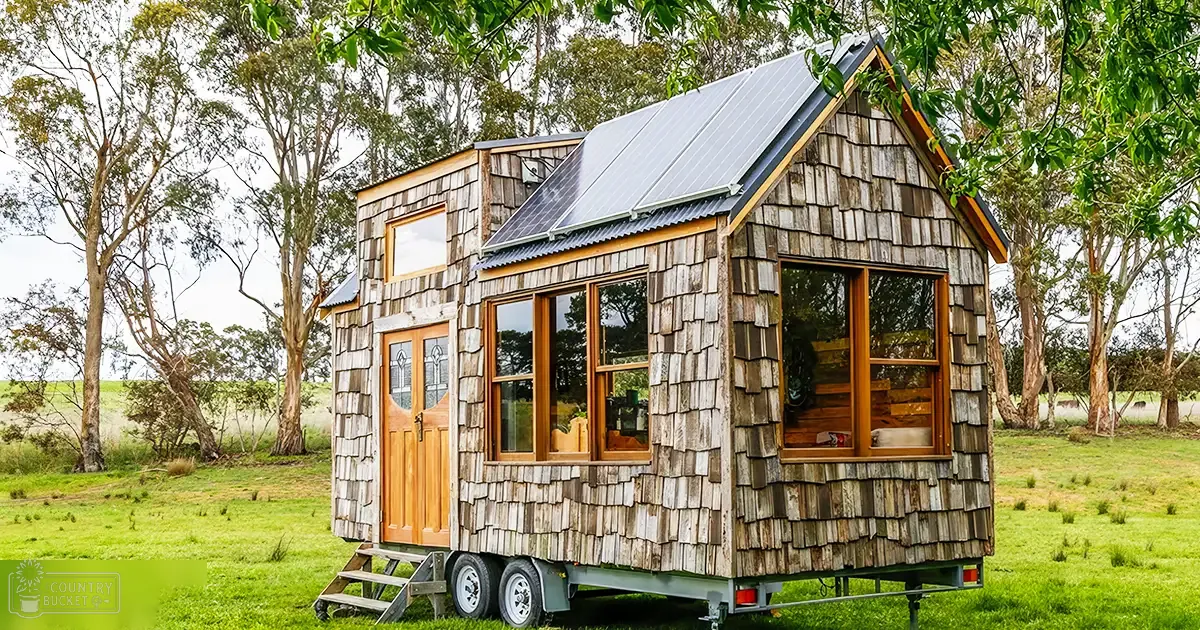 A tiny house with wooden shingles and a corrugated metal roof in a rural countryside setting.