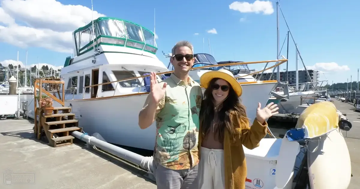 A sunny day at a marina with various boats docked, with two adults in casual attire and a wooden staircase leading up to the boat.
