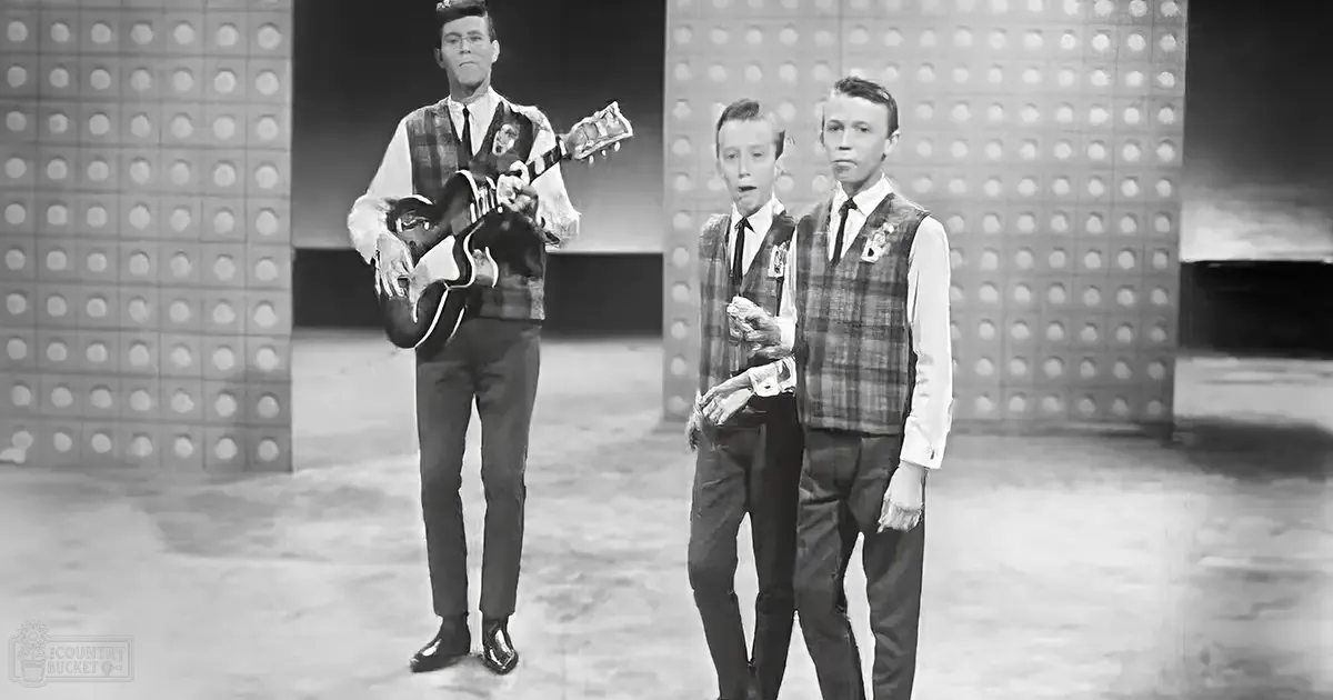 A mid-20th-century stage or studio setting with young adult males dressed formally, possibly a television show or theatrical production.