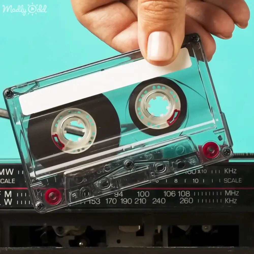 A transparent cassette tape being inserted into an old radio indoors. The radio has frequency settings for FM and MW bands.