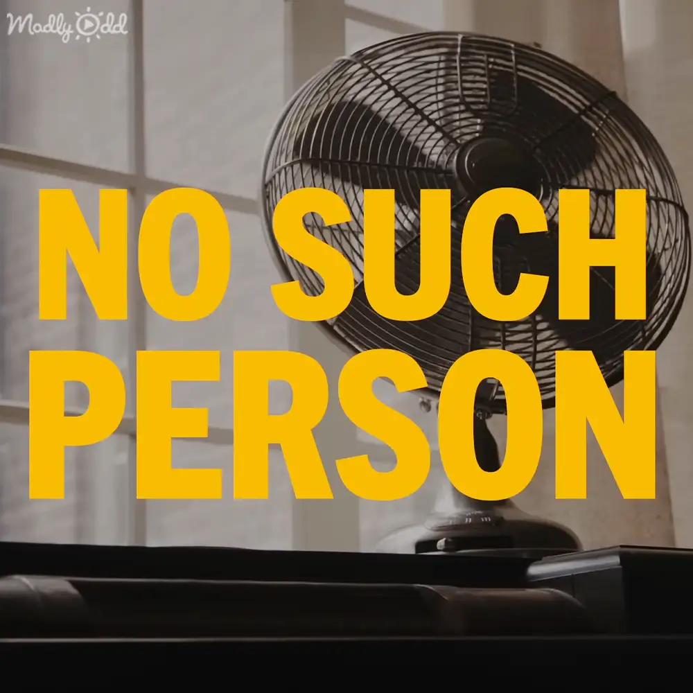 Indoor scene, oscillating floor fan with a control panel at its base; bold yellow text partially obscures it. White curtains and natural light suggest daytime.