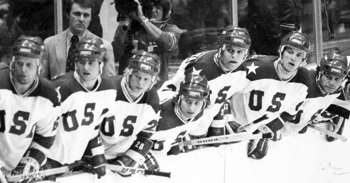 A hockey team in white jerseys with 'USA' and stars on them practicing or playing at a rink, set against the backdrop of an indoor arena under bright artificial lights.