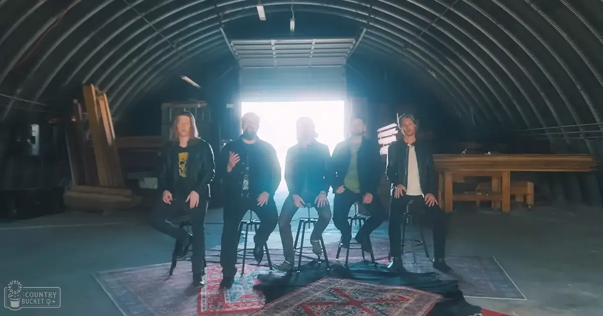 Five adults seated indoors under a large tent-like structure; each wears dark jackets over various shirts.