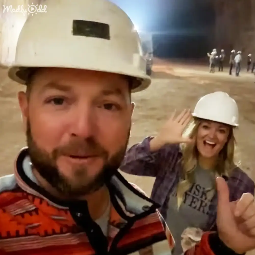 An adult male and young female construction workers wearing safety gear in an artificial-lit underground tunnel