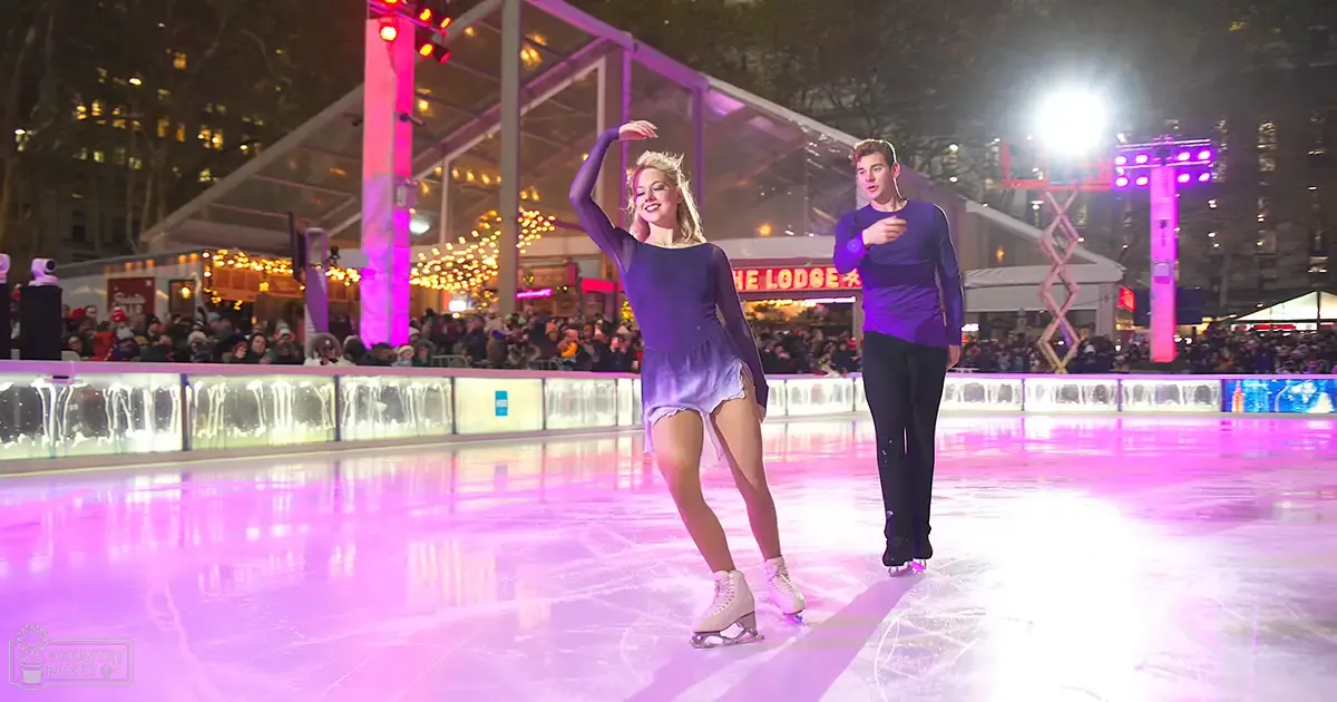 A young adult female in a purple dress skating at an outdoor rink surrounded by festive string lights, with a crowd of spectators behind her.
