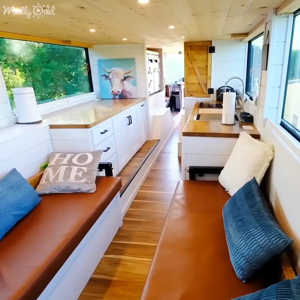 A cozy indoor space with two brown leather benches and white cabinets under large windows showing greenery outside, suggesting daytime in spring or summer.