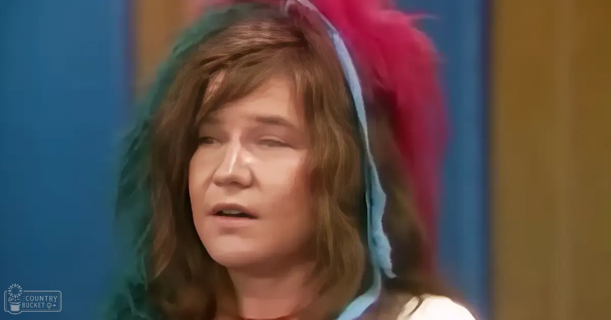Middle-aged adult female wearing a colorful feathered headpiece indoors with artificial lighting.