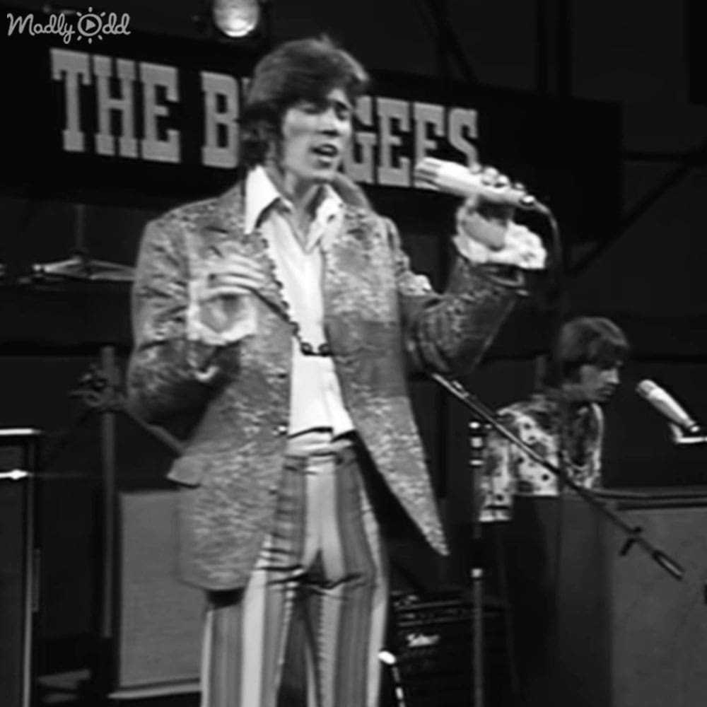 A male performer from 'The Buggles' wearing a patterned, textured jacket with wide lapel and striped pants in what appears to be a music studio or stage setup.