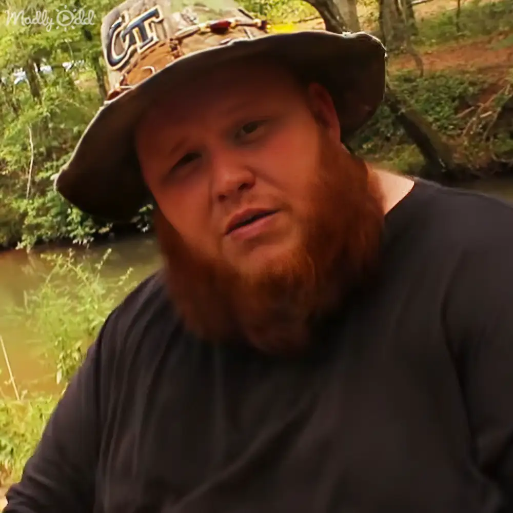 Adult male in a relaxed long-sleeved dark gray/black shirt with a wide-brimmed 'CT' printed hat outdoors among trees and greenery, late afternoon light casting warm tones.